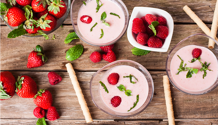 Bowls of Gluten Free Strawberry Mousse are displayed on a wooden table scattered with fresh strawberries